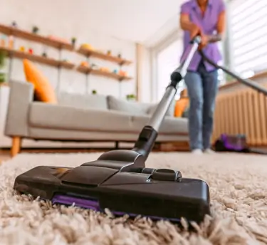 Close-up of a vacuum cleaner cleaning a carpet, suggesting dust as an allergy trigger