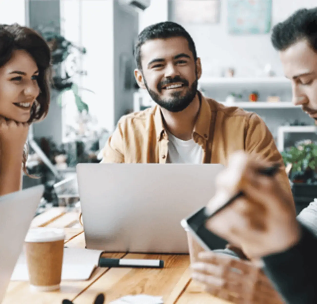 Fotografía de dos hombres y una mujer en una mesa, donde hay tres laptops, una pluma, un par de libretas y un vaso.