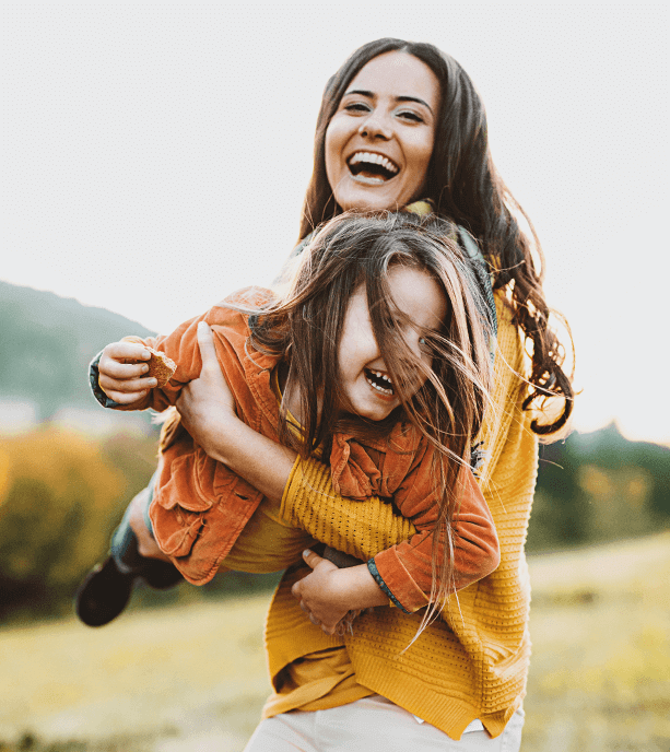 Fotografía de una mujer cargando a una niña, ambas sonríen.
